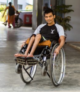 a young man sits in a wheelchair with the chair tipped backwards. He is in the entrance to the rehab institute at CMC Vellore.
